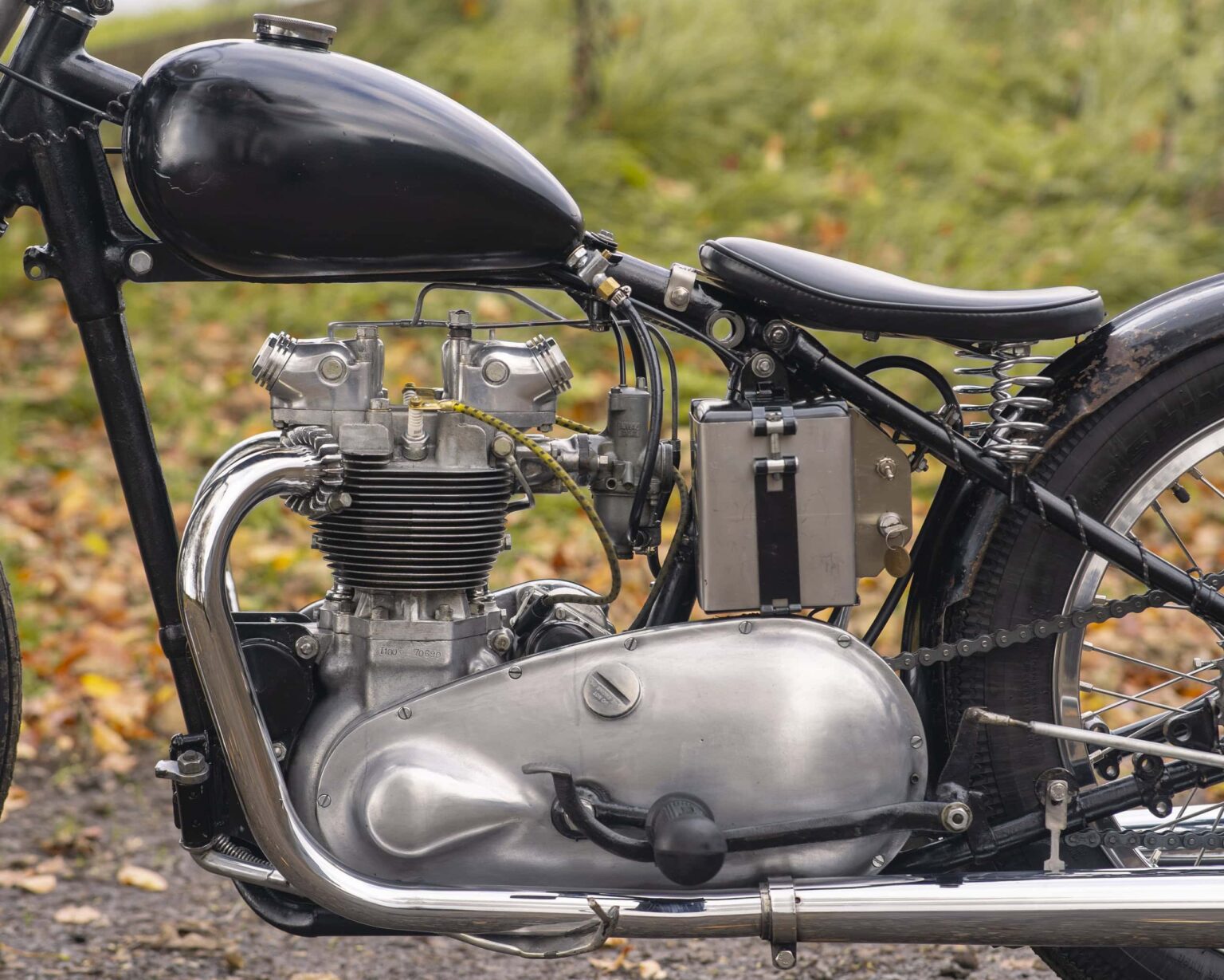 Close-up of vintage motorcycle engine with classic metal parts, set outdoors on a leaf-covered ground.