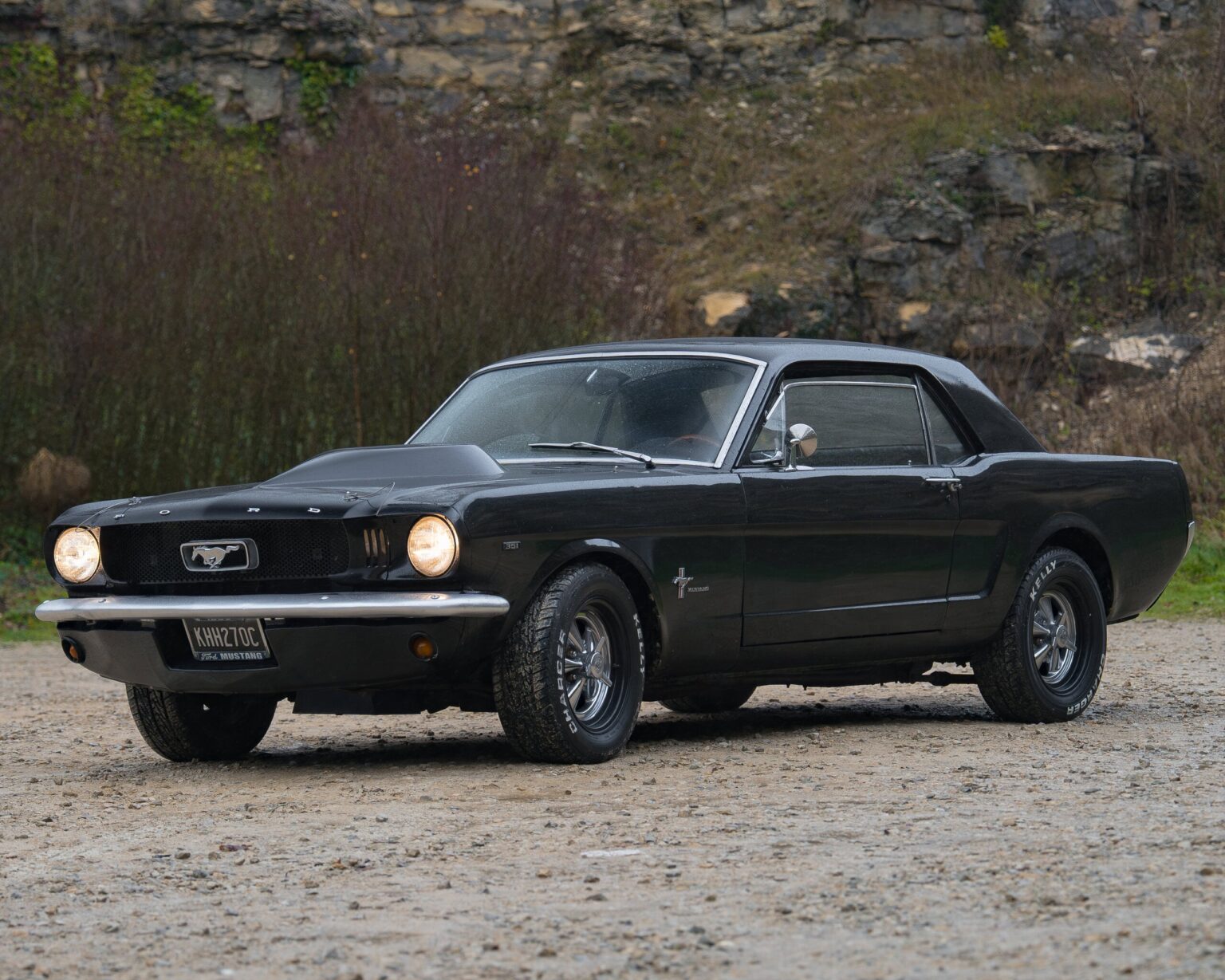 Black classic Ford Mustang parked outdoors with rugged background.