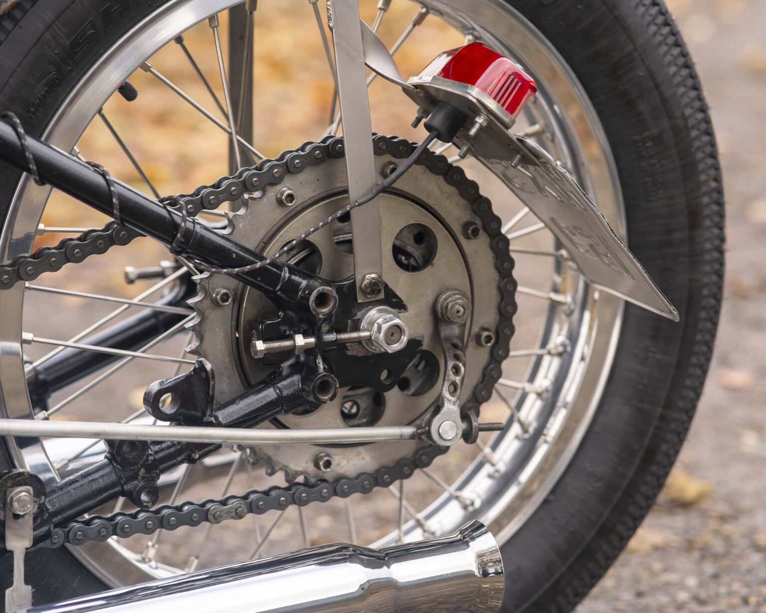 Close-up of classic motorcycle rear wheel, chain, and gear system, showcasing vintage engineering and design.