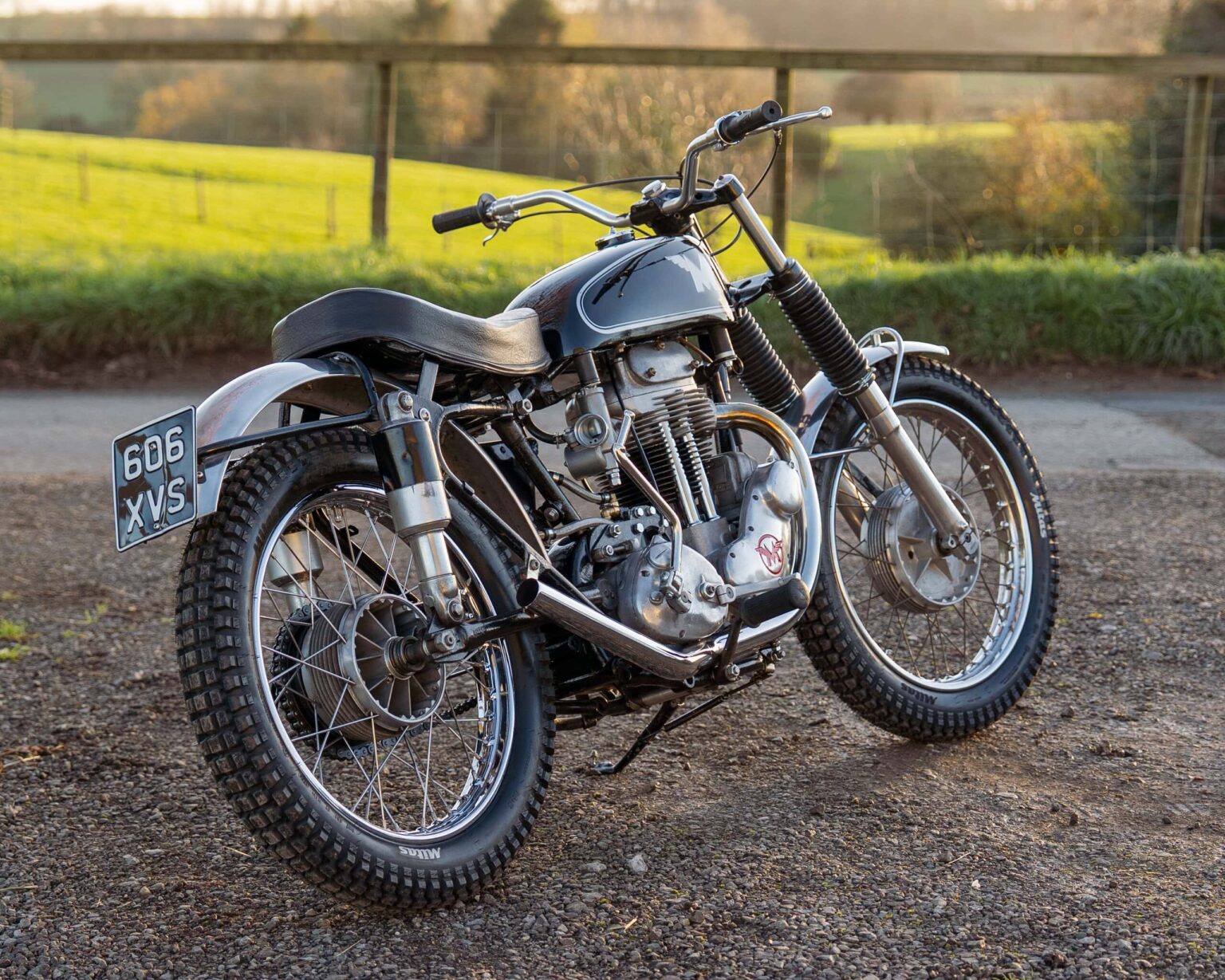 Vintage motorcycle with classic design and rugged tires, parked outdoors at a classic car event.