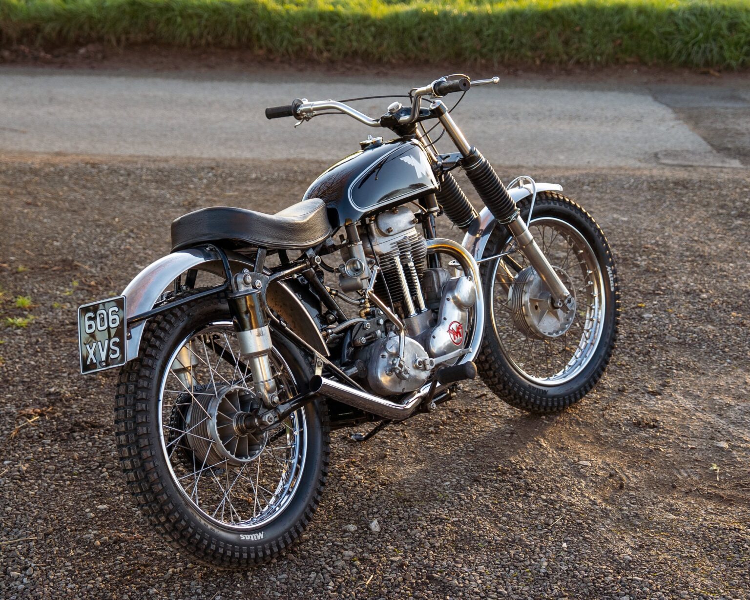 Classic vintage motorcycle with black and chrome finish, detailed engine and spoked wheels on gravel surface.