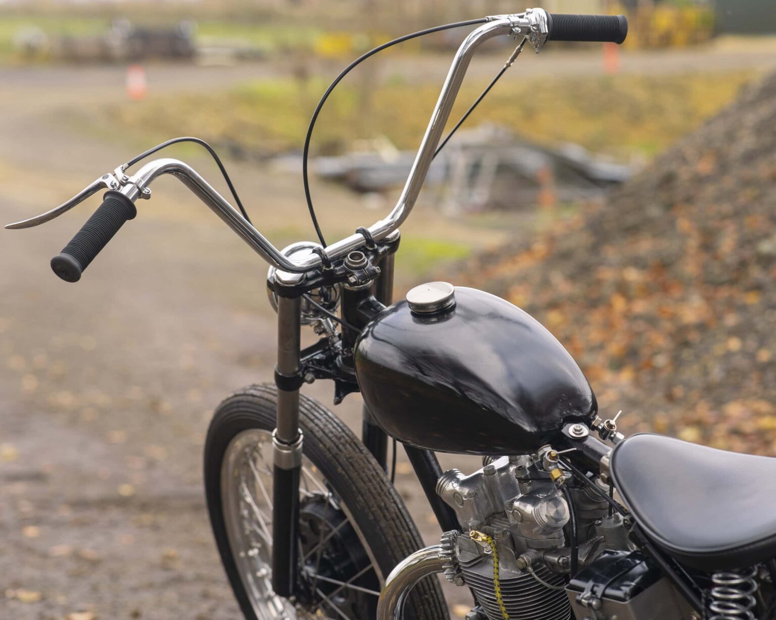 Classic custom-built motorcycle featuring a black fuel tank and chrome handlebars, set against autumn scenery.