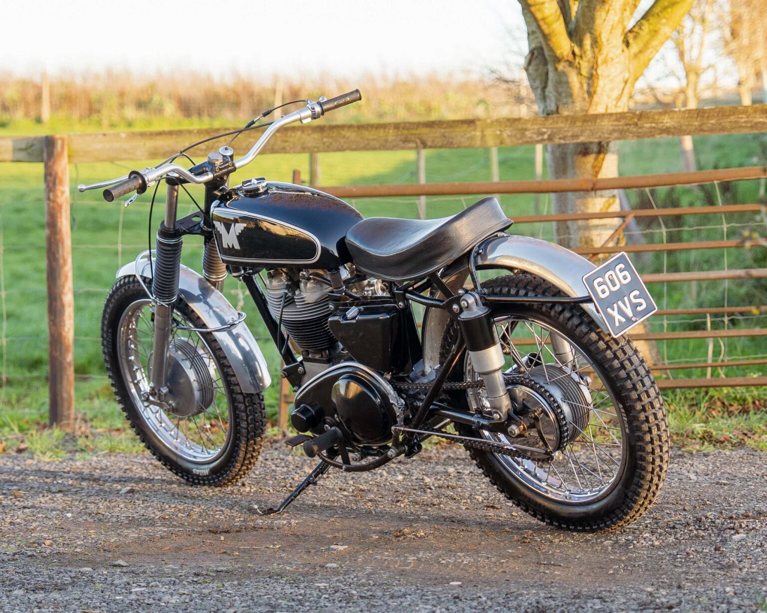 Black and silver vintage motorcycle parked outdoors on gravel, perfect for vintage motorcycle enthusiasts.