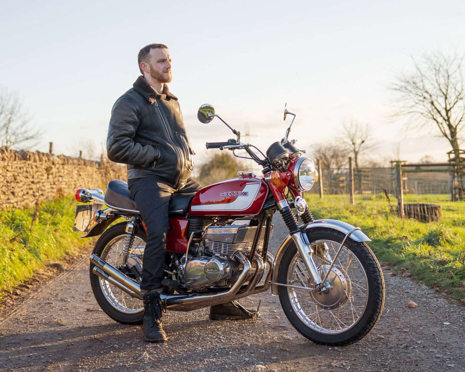 Vintage Suzuki motorcycle with rider in outdoor rural setting.
