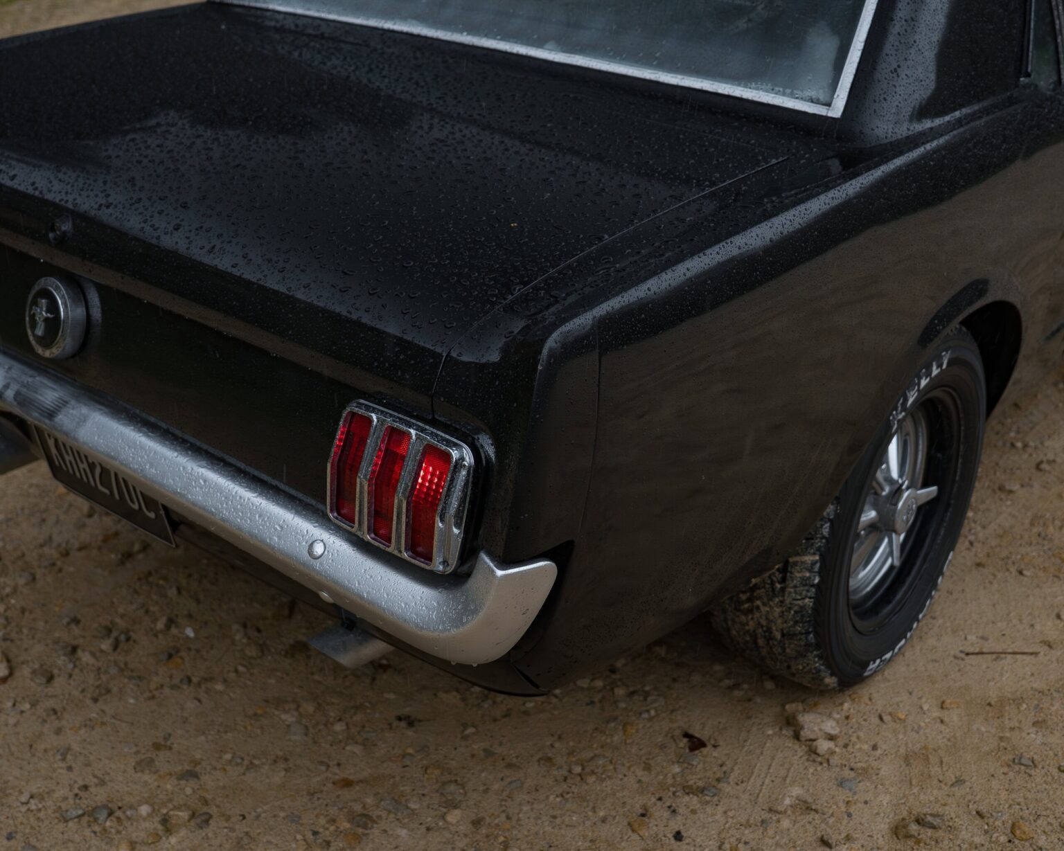 Close-up of a vintage black classic car with raindrops, showing the rear lights, bumper, and tyre detail.