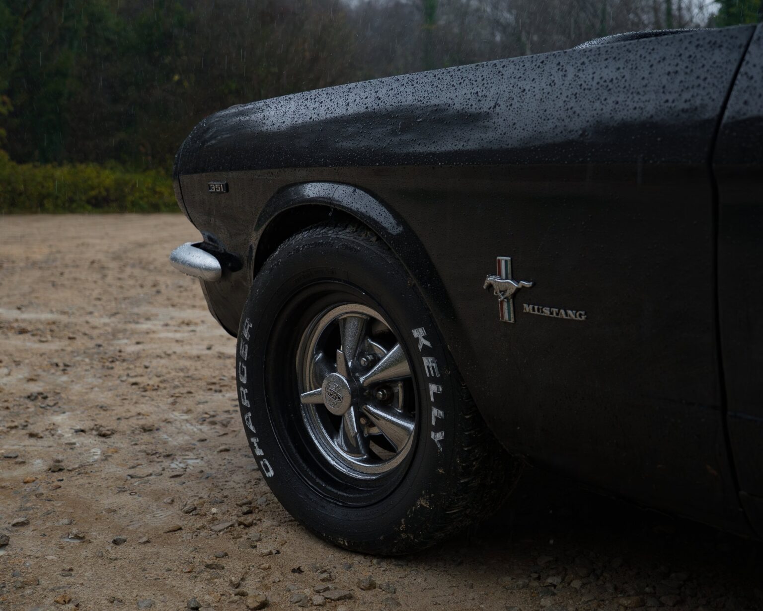 Classic Ford Mustang wheel and tire on a wet, outdoor surface.
