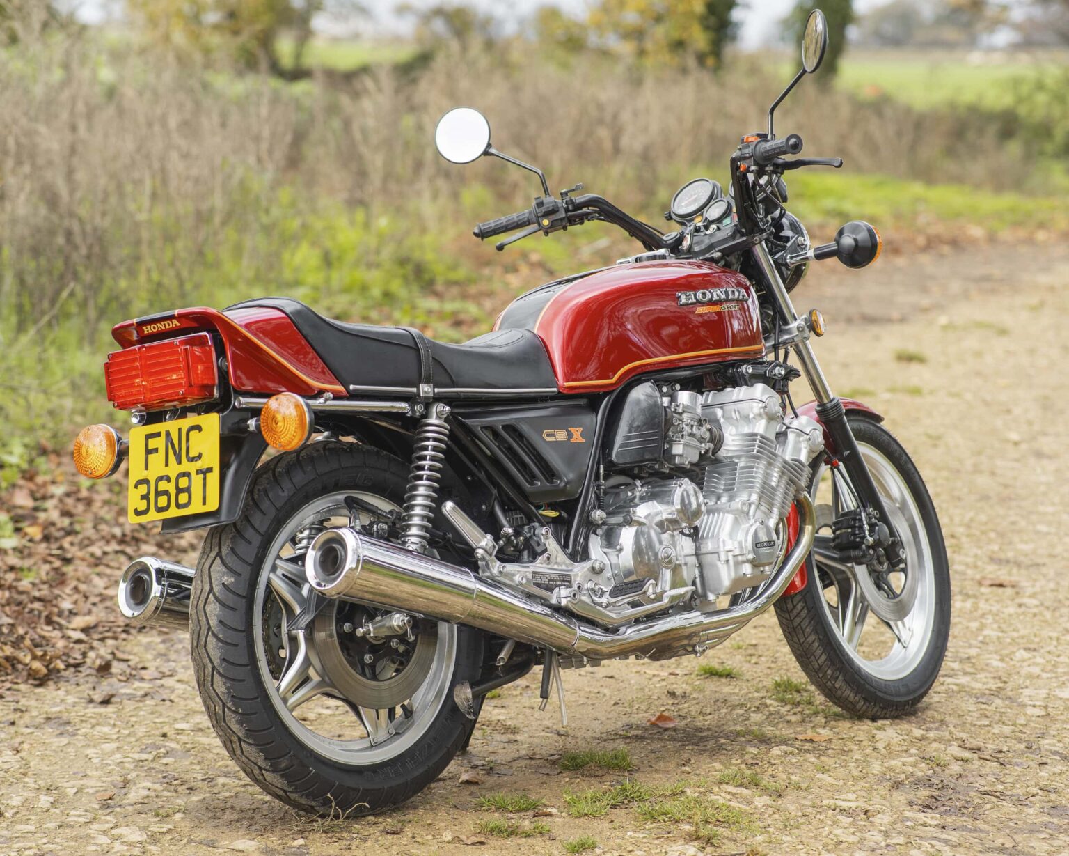 Vintage Honda CBX motorcycle with red paint and chrome details on a gravel track outdoors.