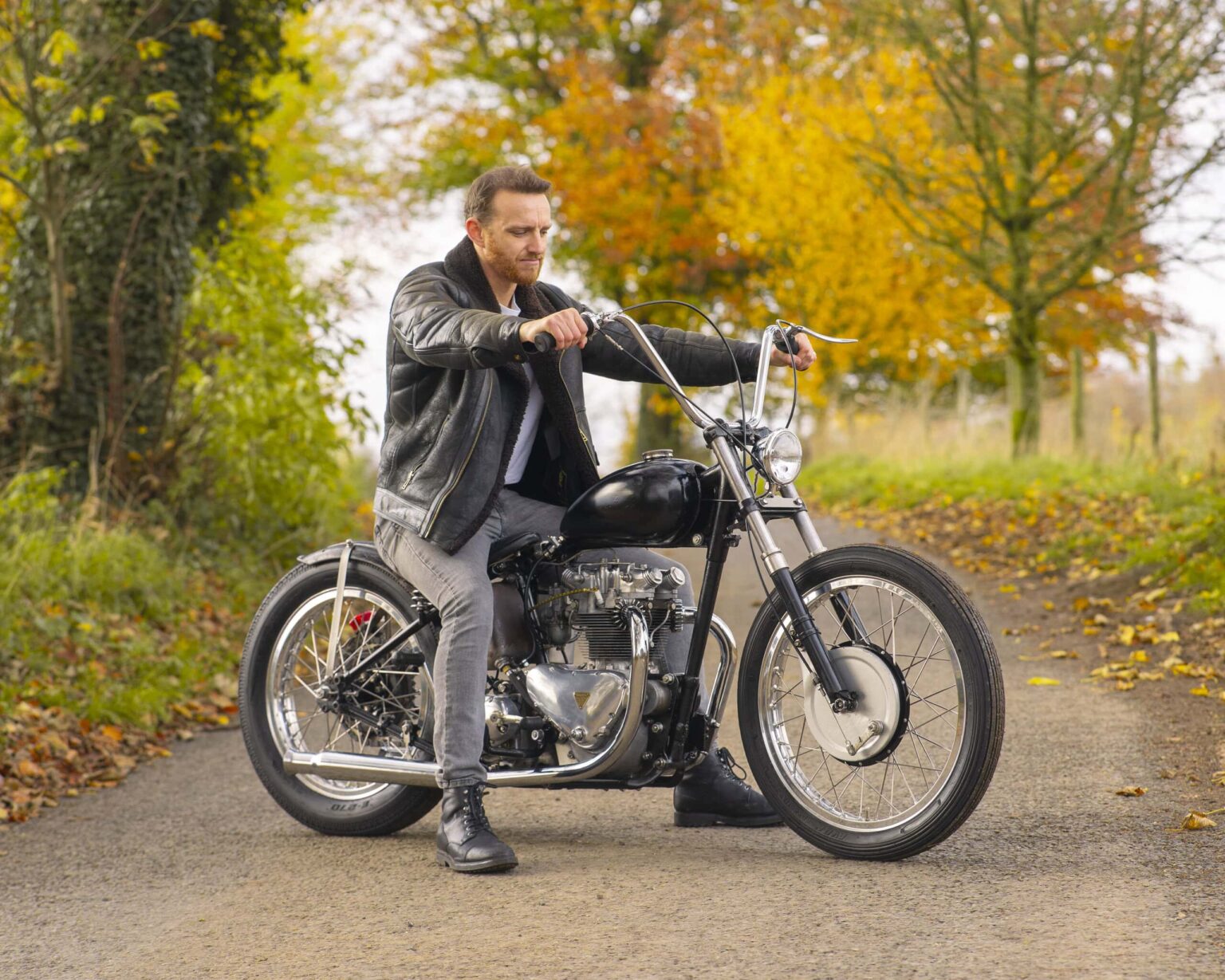 Man riding vintage motorcycle on autumn countryside road.