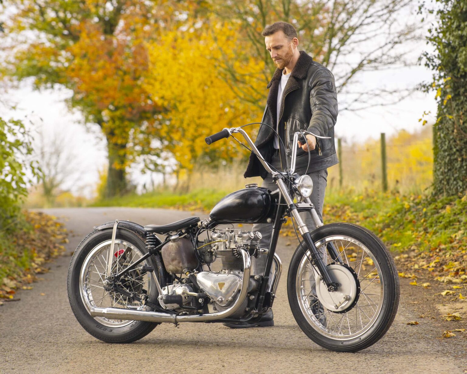 Man with vintage motorcycle in autumn landscape, showing retro motorcycle style.