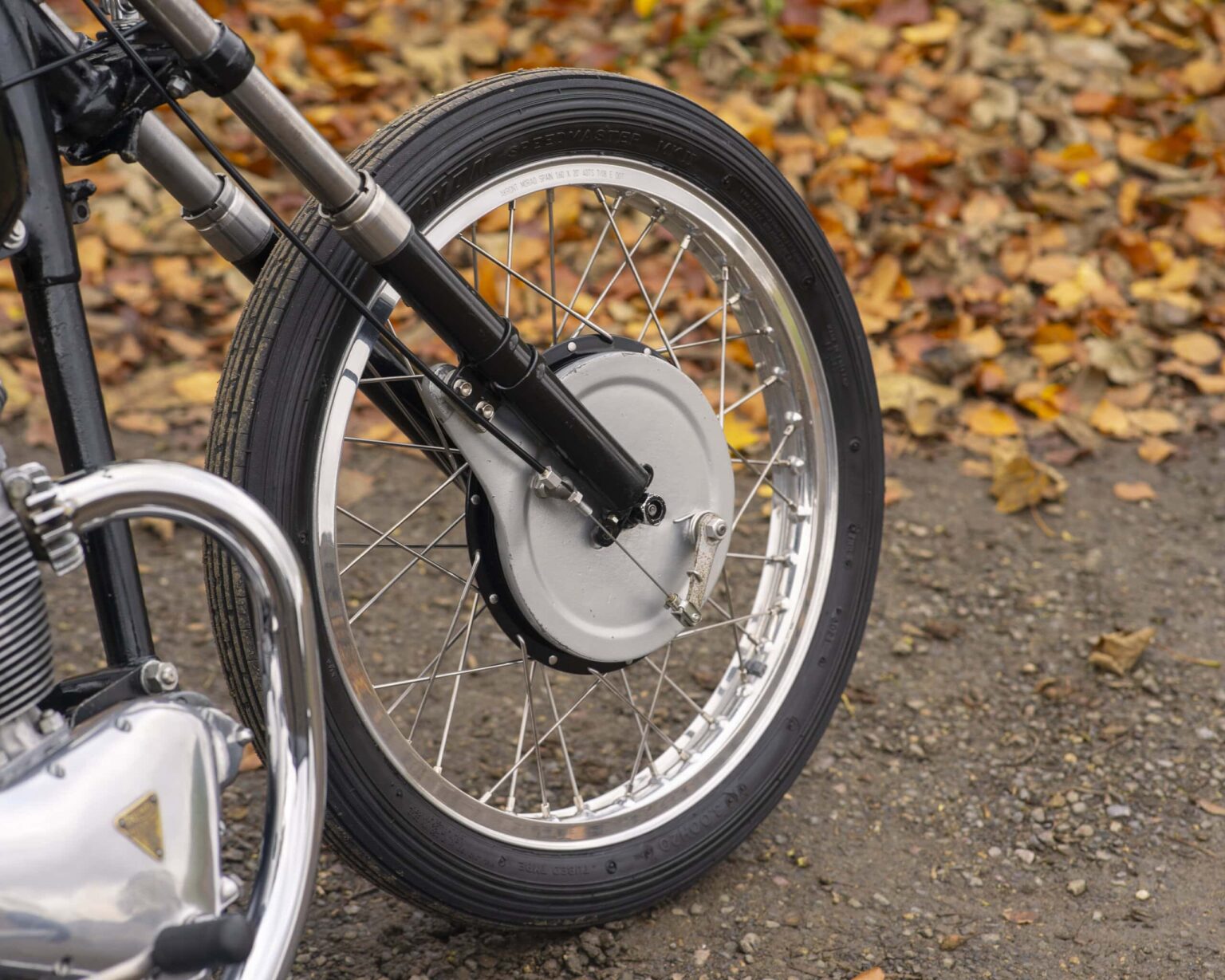 Close-up of vintage motorcycle front wheel with spokes and tyre on autumn leaves background.