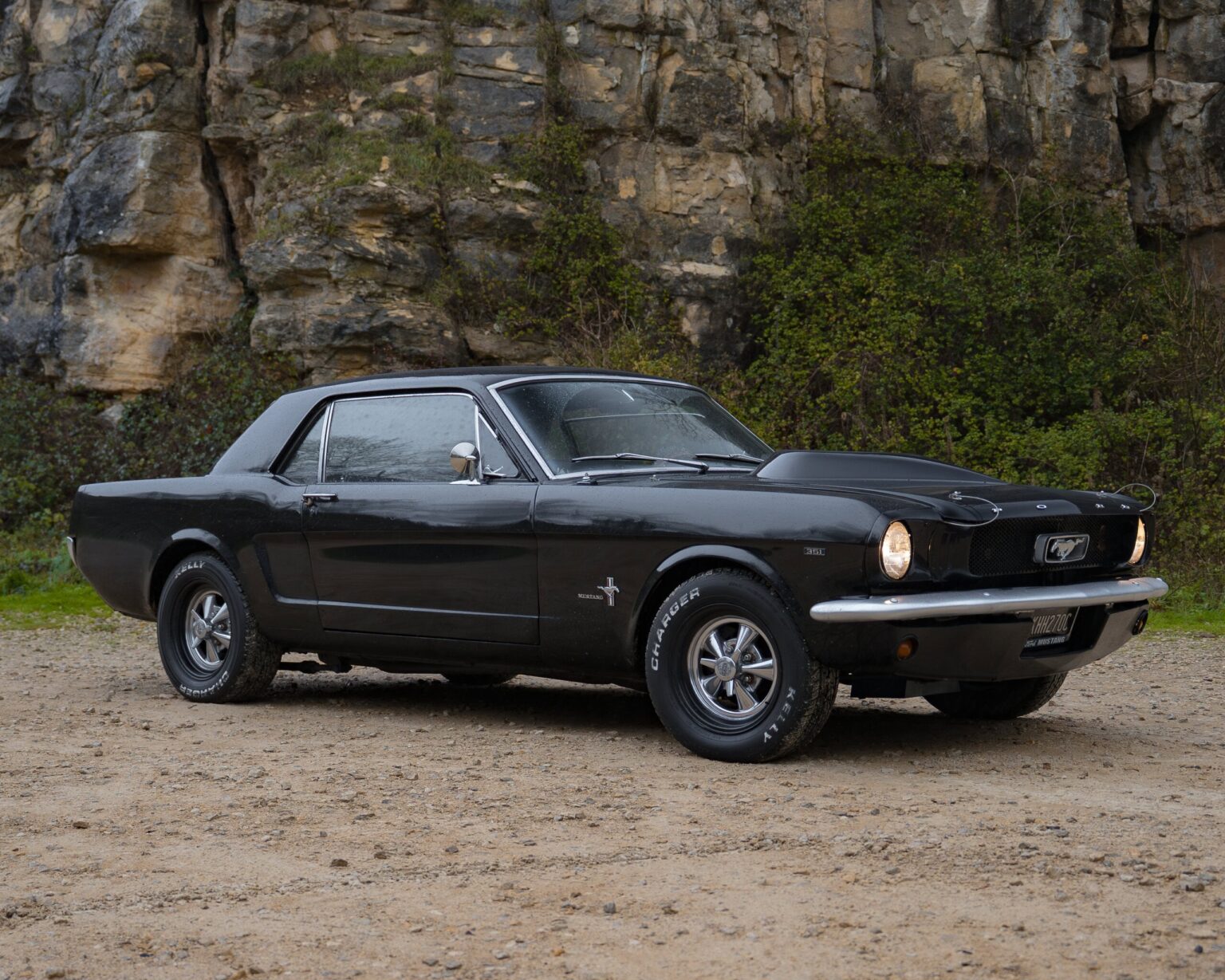 Black vintage Ford Mustang parked outdoors on a dirt surface.