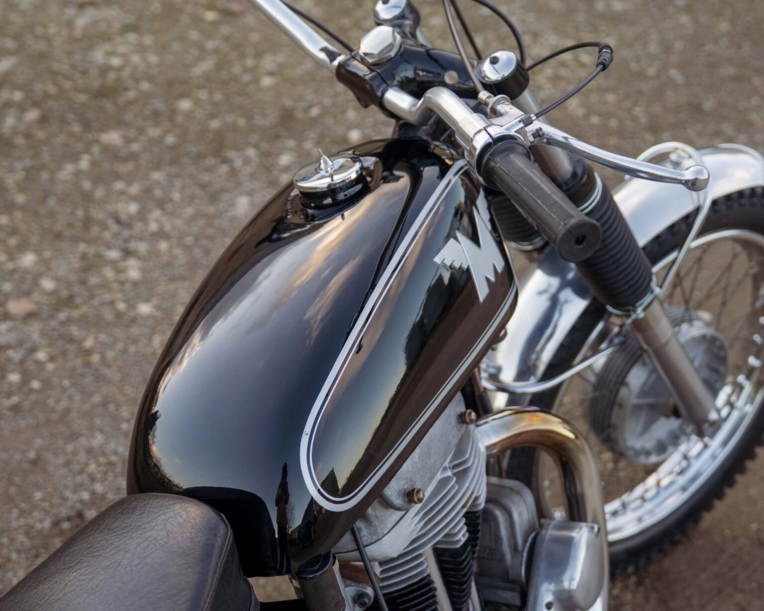 Detailed view of a classic vintage motorcycle, showcasing black and chrome elements, at a classic bike show.