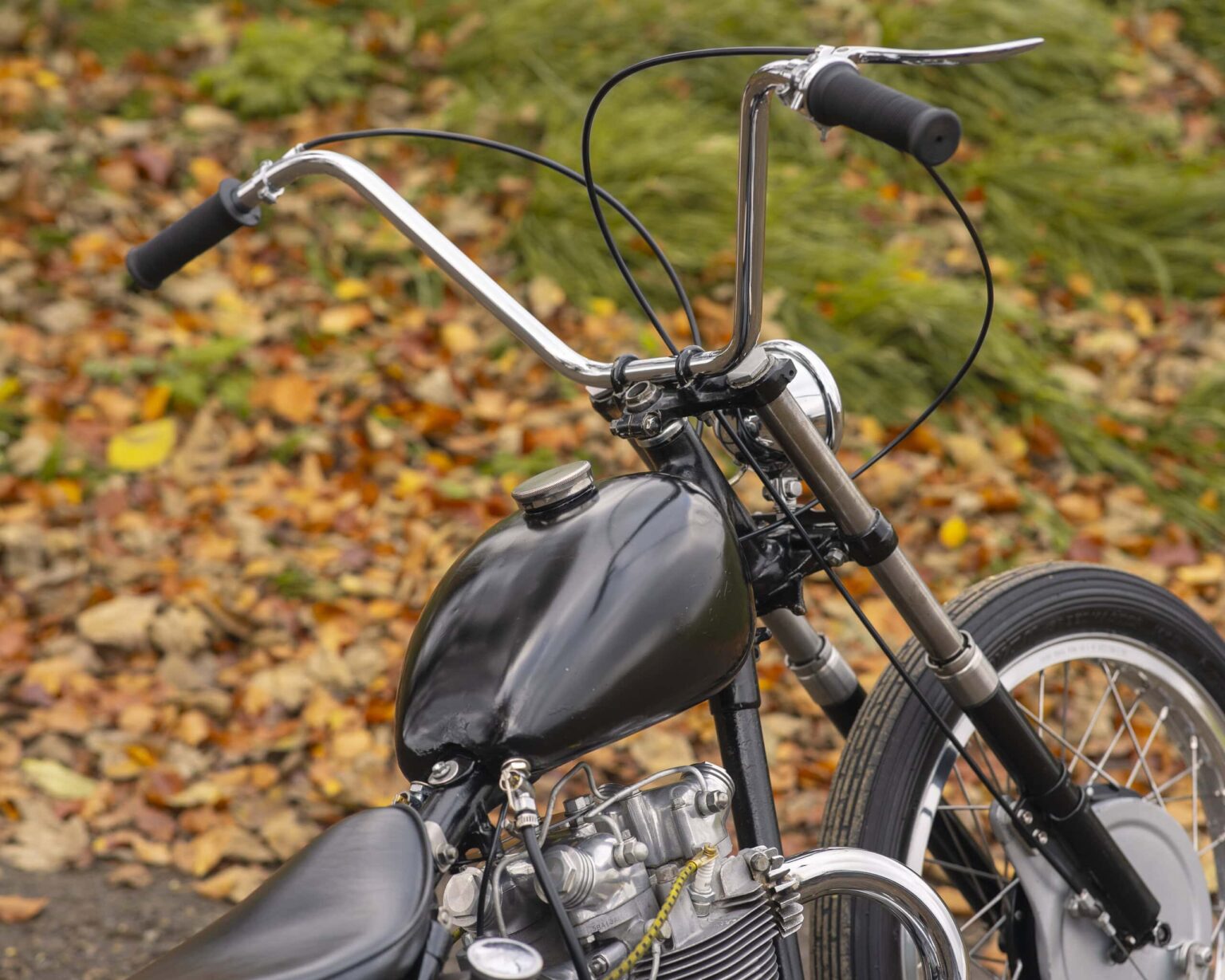 Classic black motorcycle frame with engine and handlebars on autumn leaves.