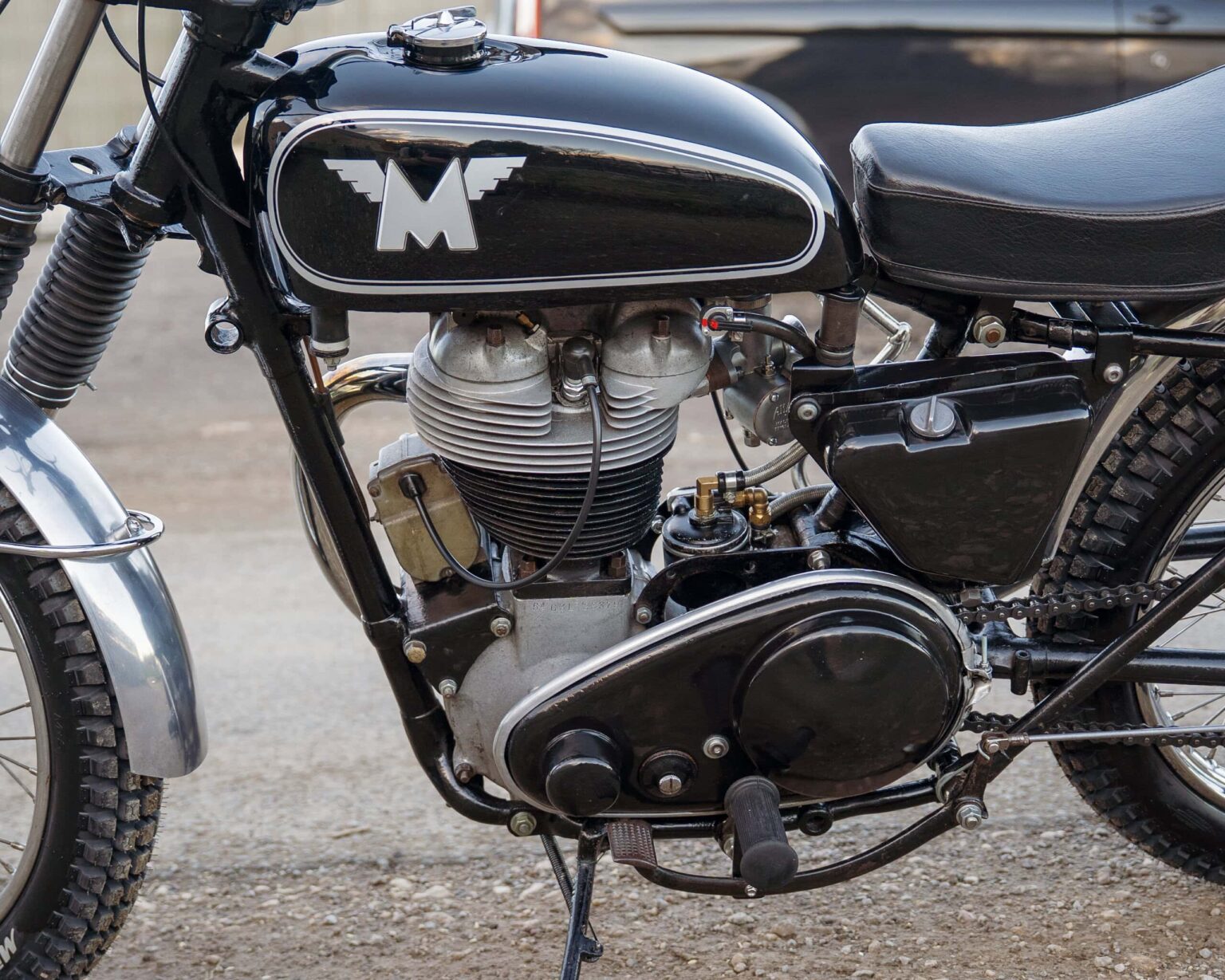 Close-up of a vintage motorcycle engine with black tank, metallic details, and rugged tires.