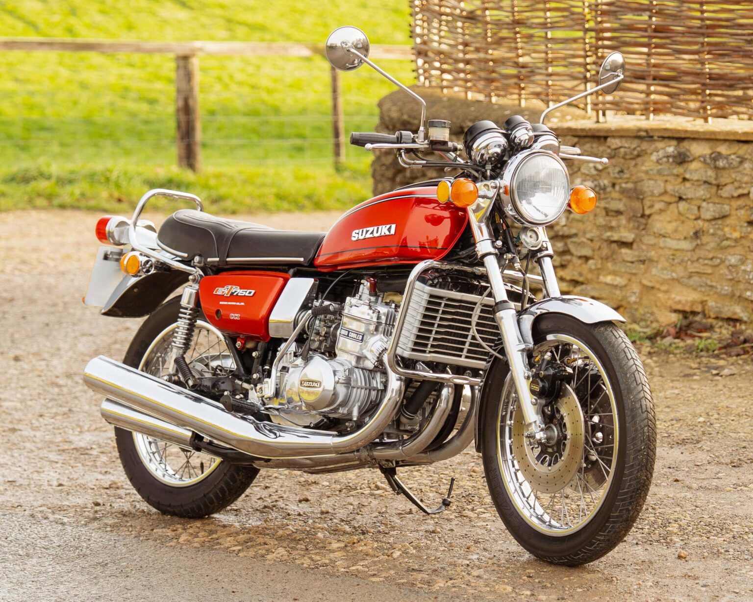 Vintage Suzuki GT750 motorcycle in red with chrome parts on gravel surface.