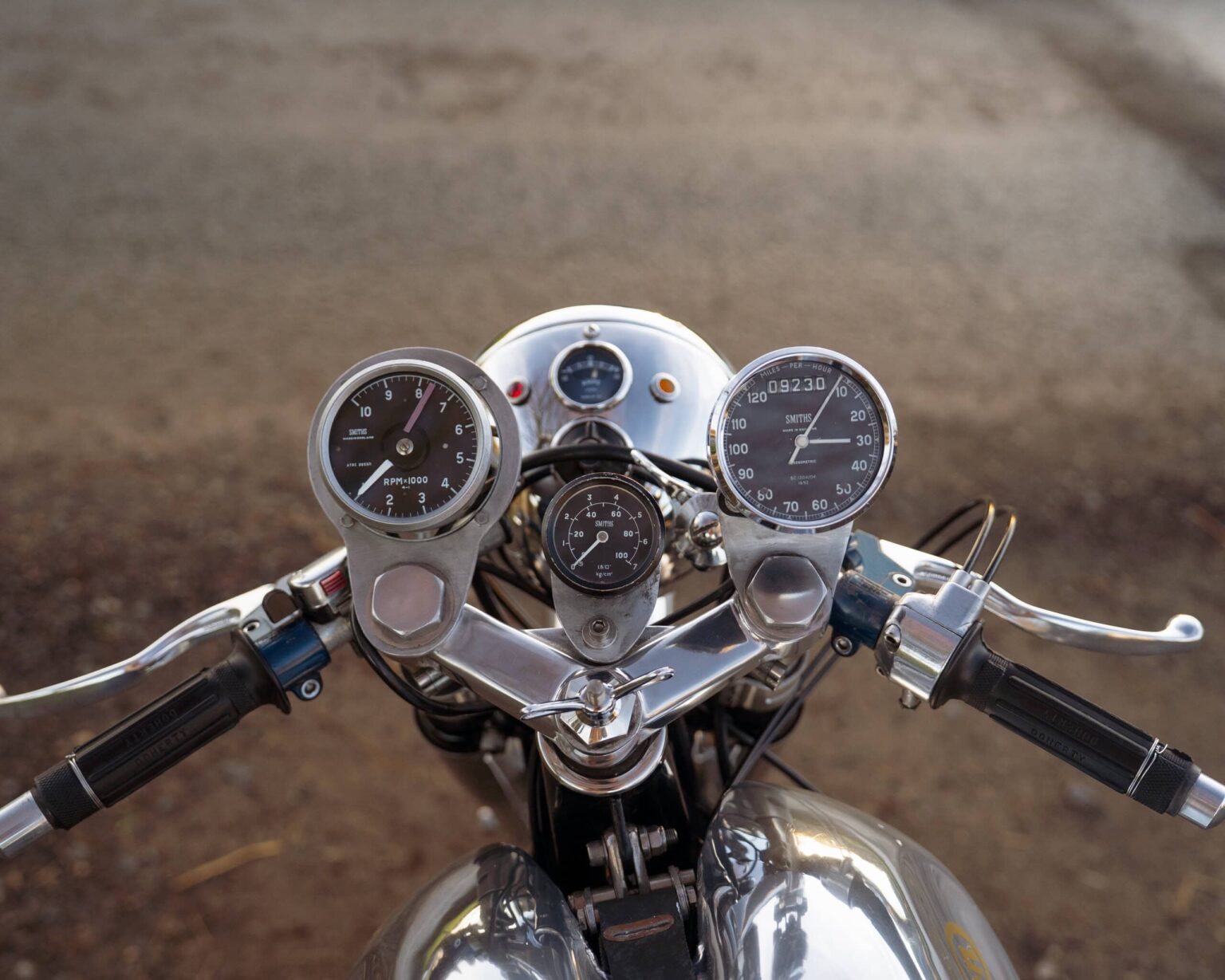 Motorcycle dashboard with chrome finish, vintage gauges, and odometer reading 9230 miles.