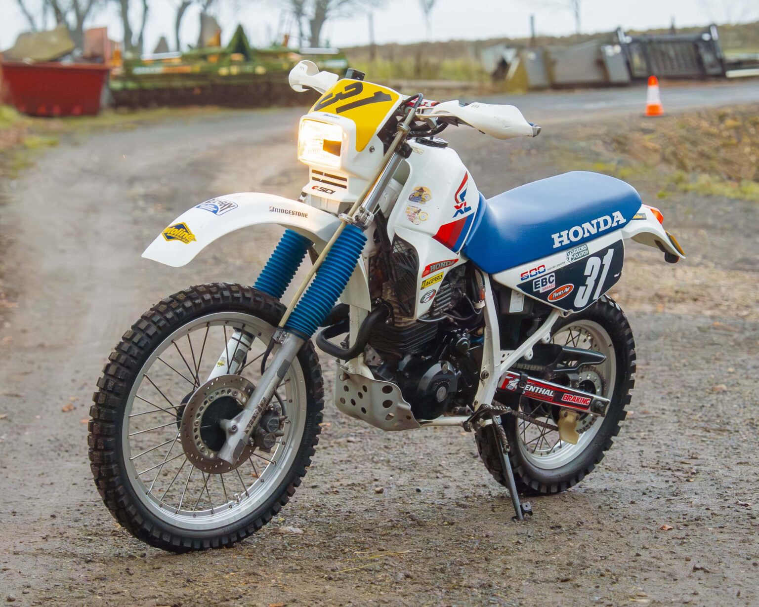 Honda dirt bike racing motorcycle, white and blue, with racing number 37, on a gravel track.