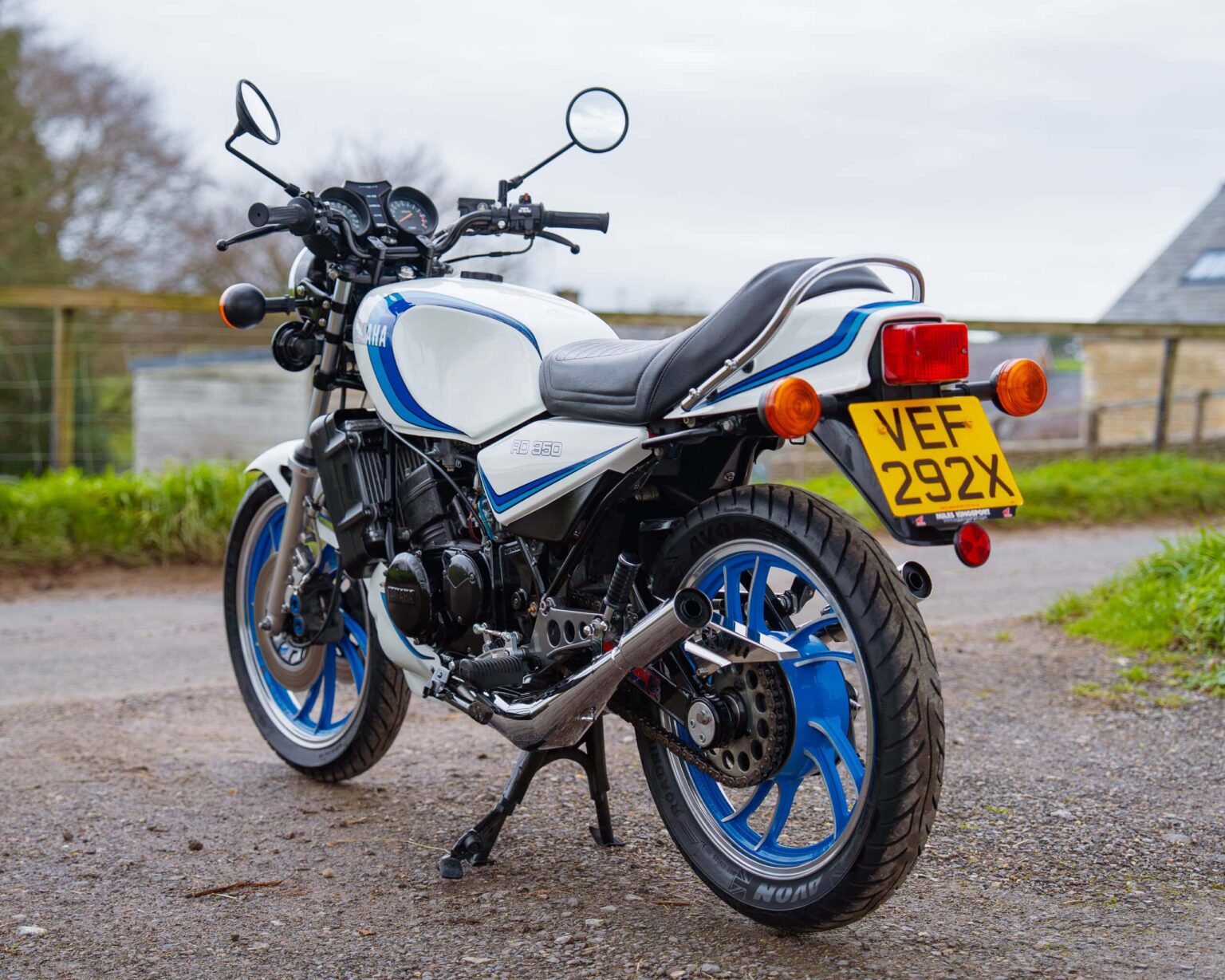 Vintage Yamaha RD350 motorcycle with blue and white colour scheme, parked outdoors on a gravel surface.