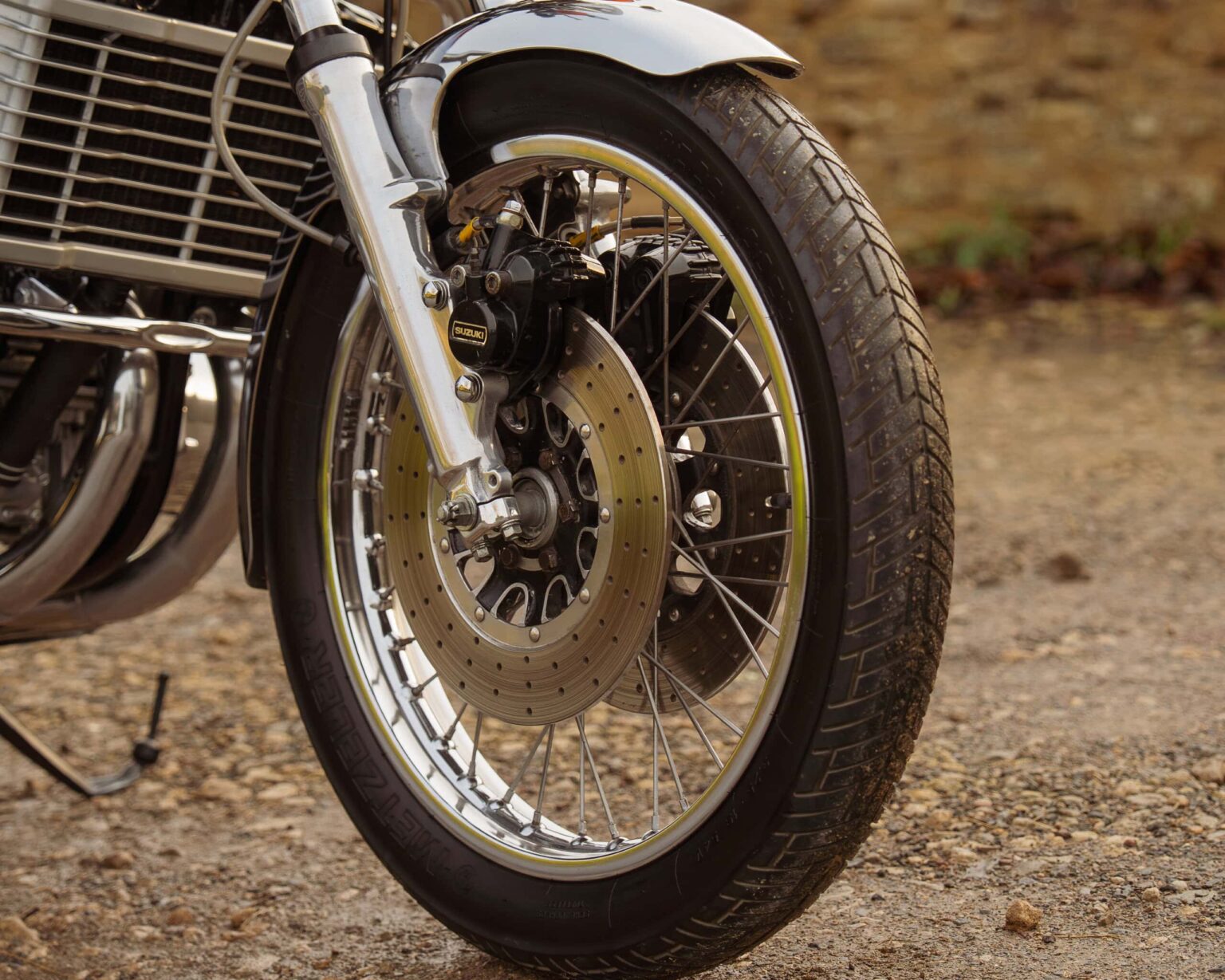 Close-up of vintage motorcycle front wheel with disc brake and wire spokes.