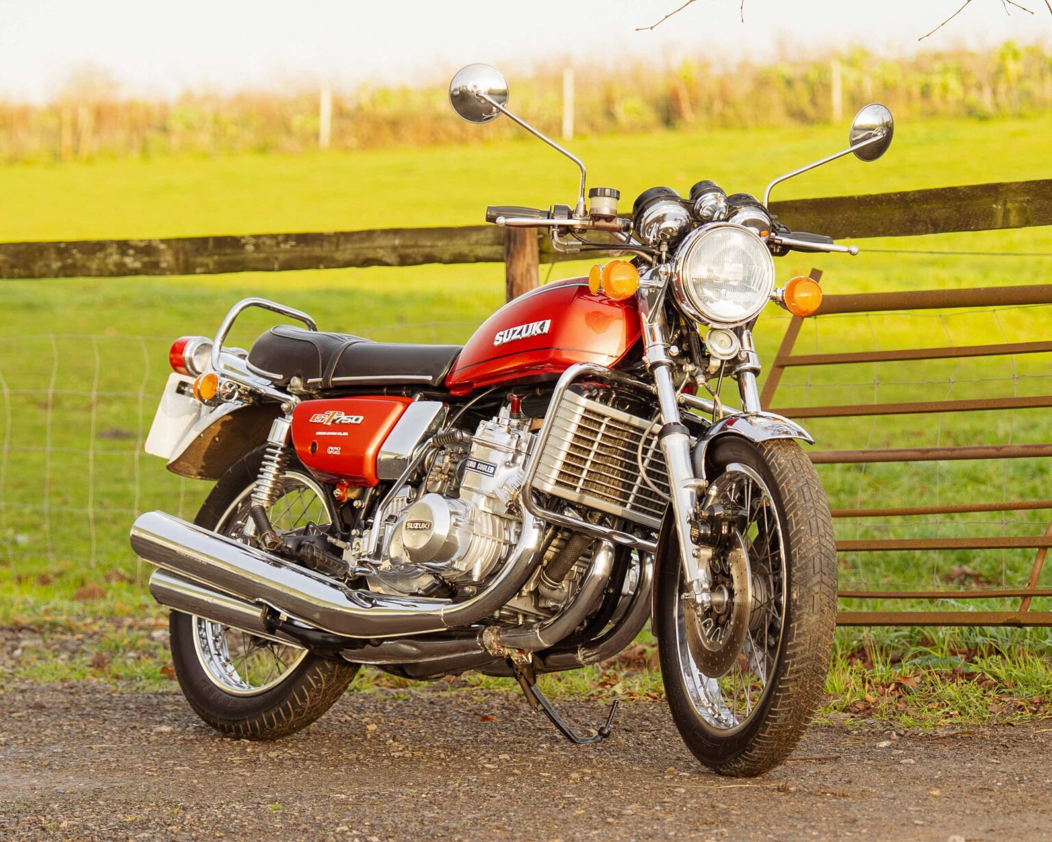 Classic red Suzuki motorcycle parked outdoors with rural background.