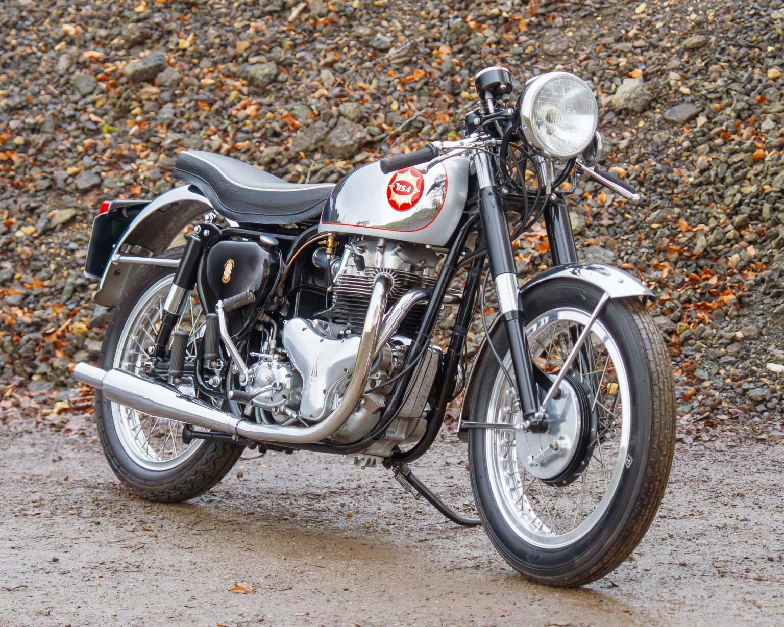 Classic British motorcycle with polished chrome and vintage design on a gravel background.