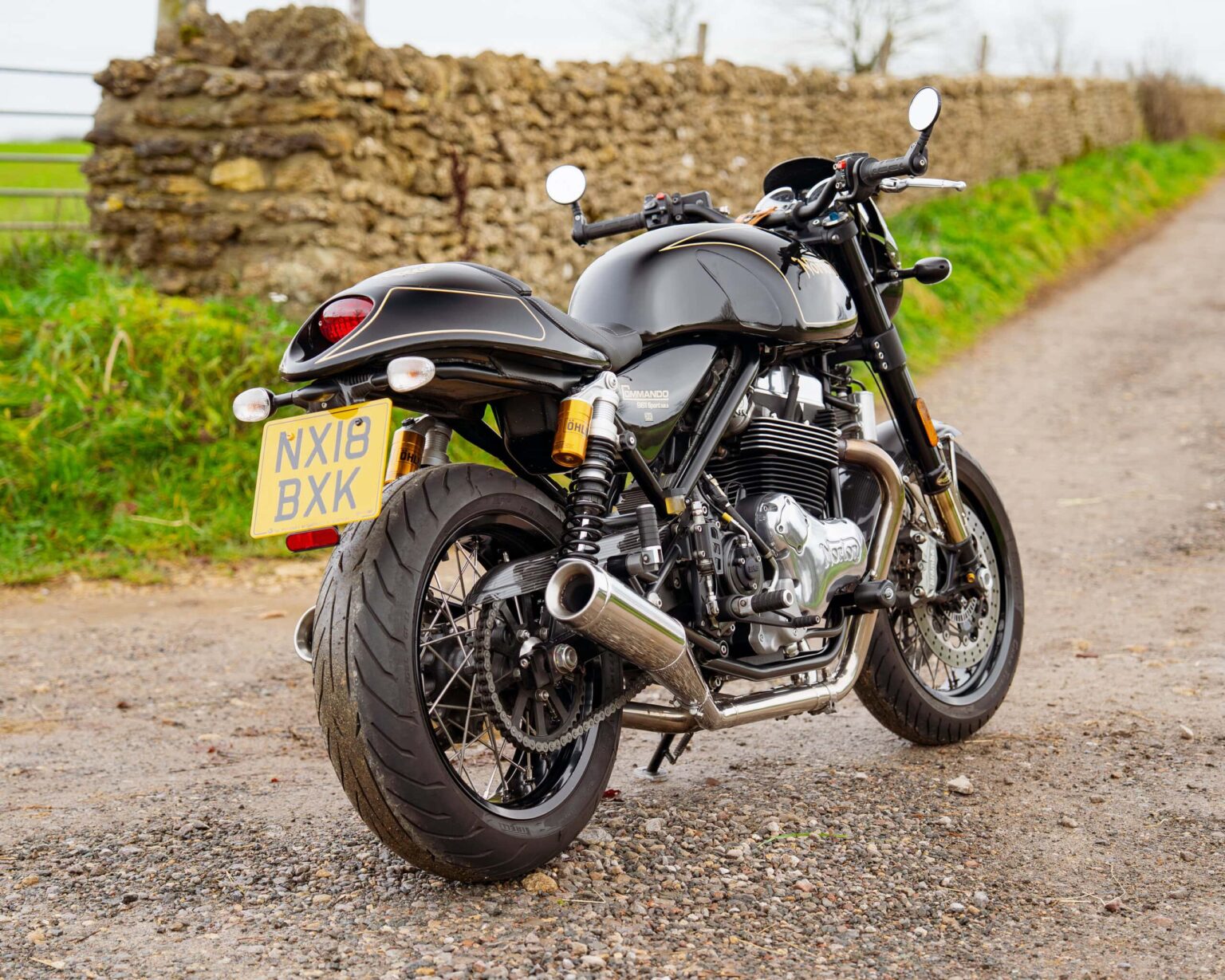 Motorcycle with black finish parked on gravel road with stone wall background.