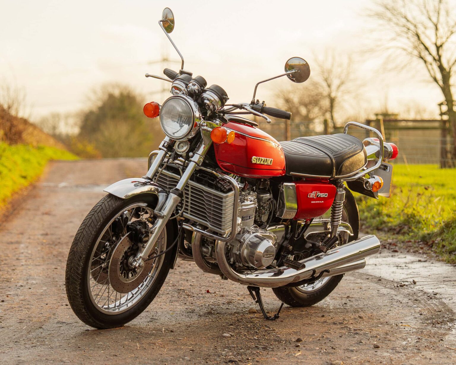 Stunning vintage Suzuki GT750 motorcycle parked on a country road. Classic design with chrome details and red paint.