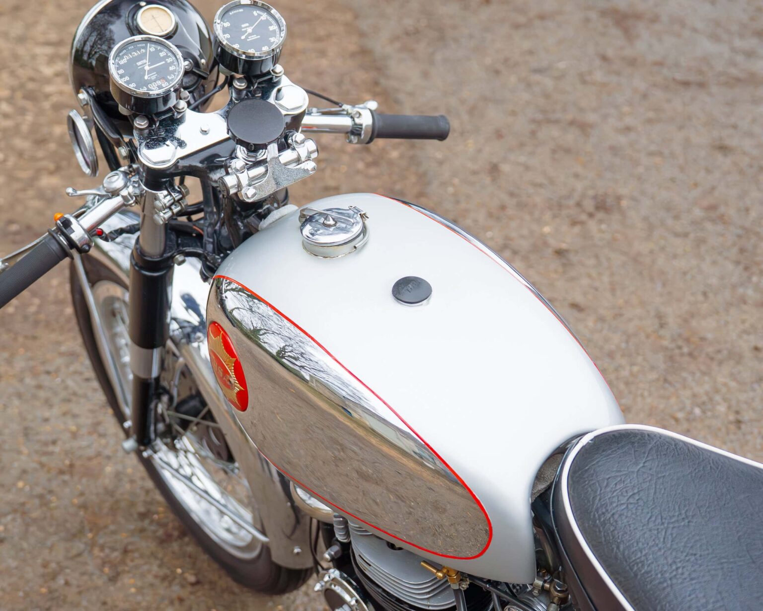 A vintage racing motorcycle with a white and chrome finish, detailed speedometer gauges, and a black leather seat.