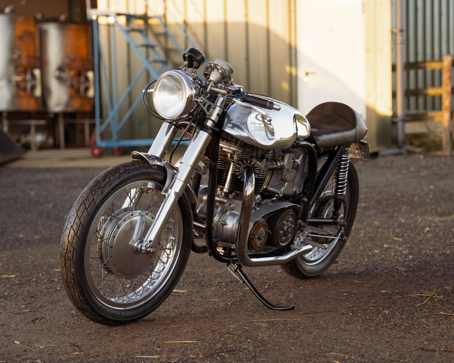 Classic motorcycle with a polished metal finish on a gravel surface outdoors.
