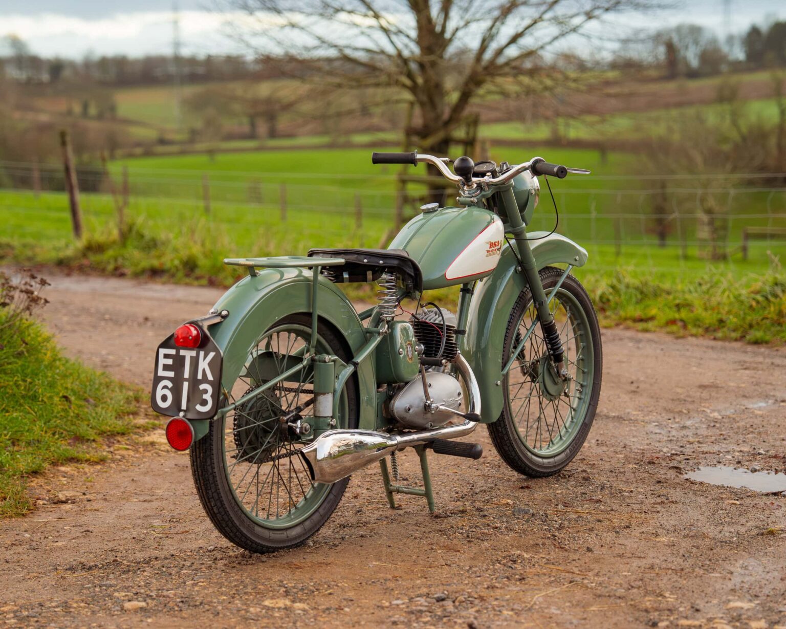 Classic vintage motorcycle with a green body and black seat, parked on a dirt path.