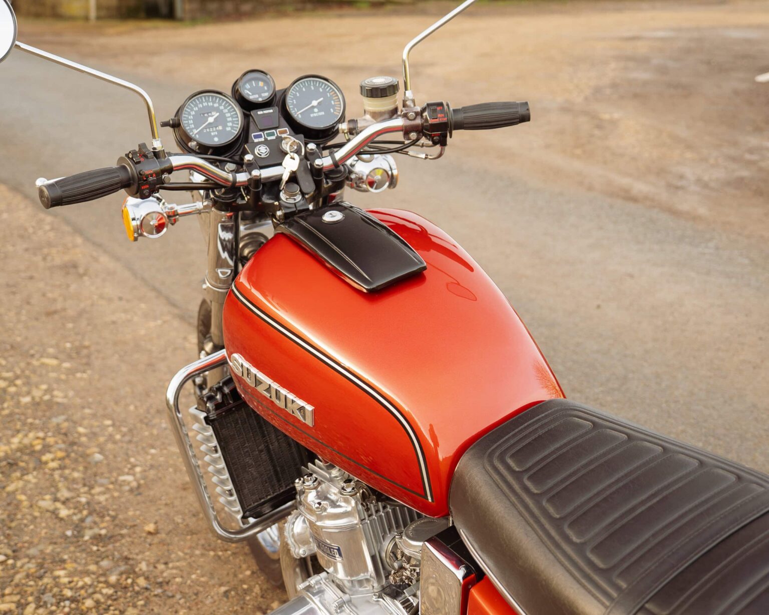 Close-up of vintage red Suzuki bike with classic gauges and black seat on rugged outdoor surface.
