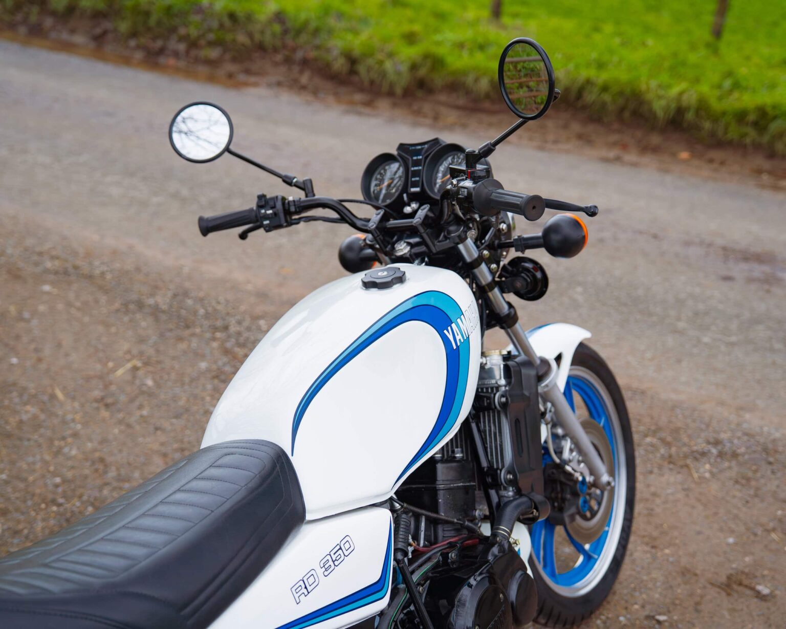 Vintage Yamaha RD 350 sportbike with white and blue colour scheme parked on gravel.