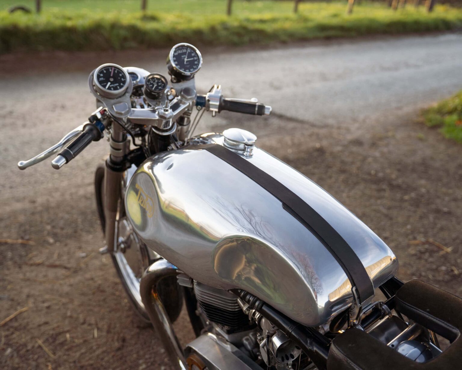 Close-up of a vintage Triumph motorcycle with chrome tank and analog dials on a rural pathway.