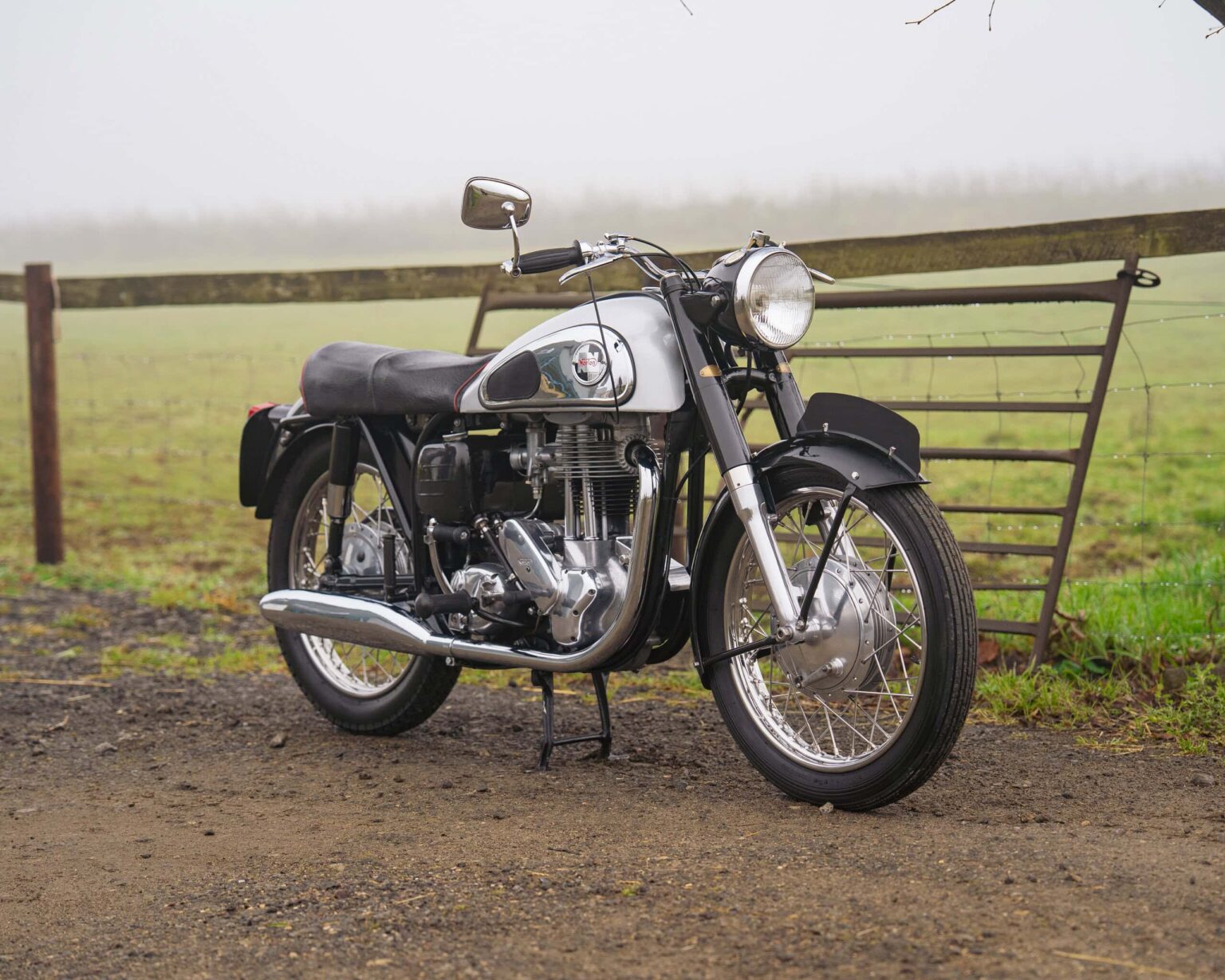 Motorcycle parked on a dirt path with a rural fence in the background.