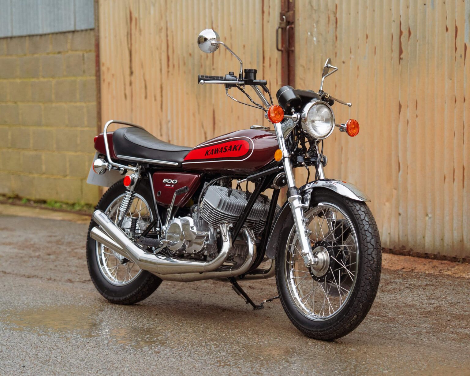 Vintage Kawasaki motorcycle parked outdoors near a wooden fence.