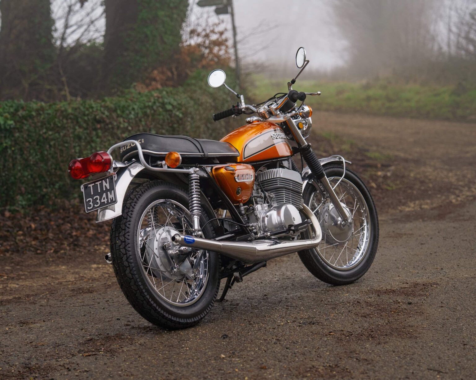 Vintage orange motorcycle parked on a foggy country road.