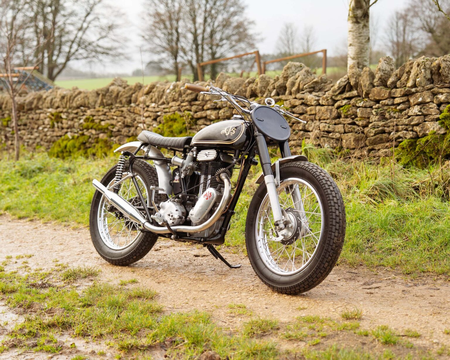 Motorcycle parked on rural country road with stone wall background.