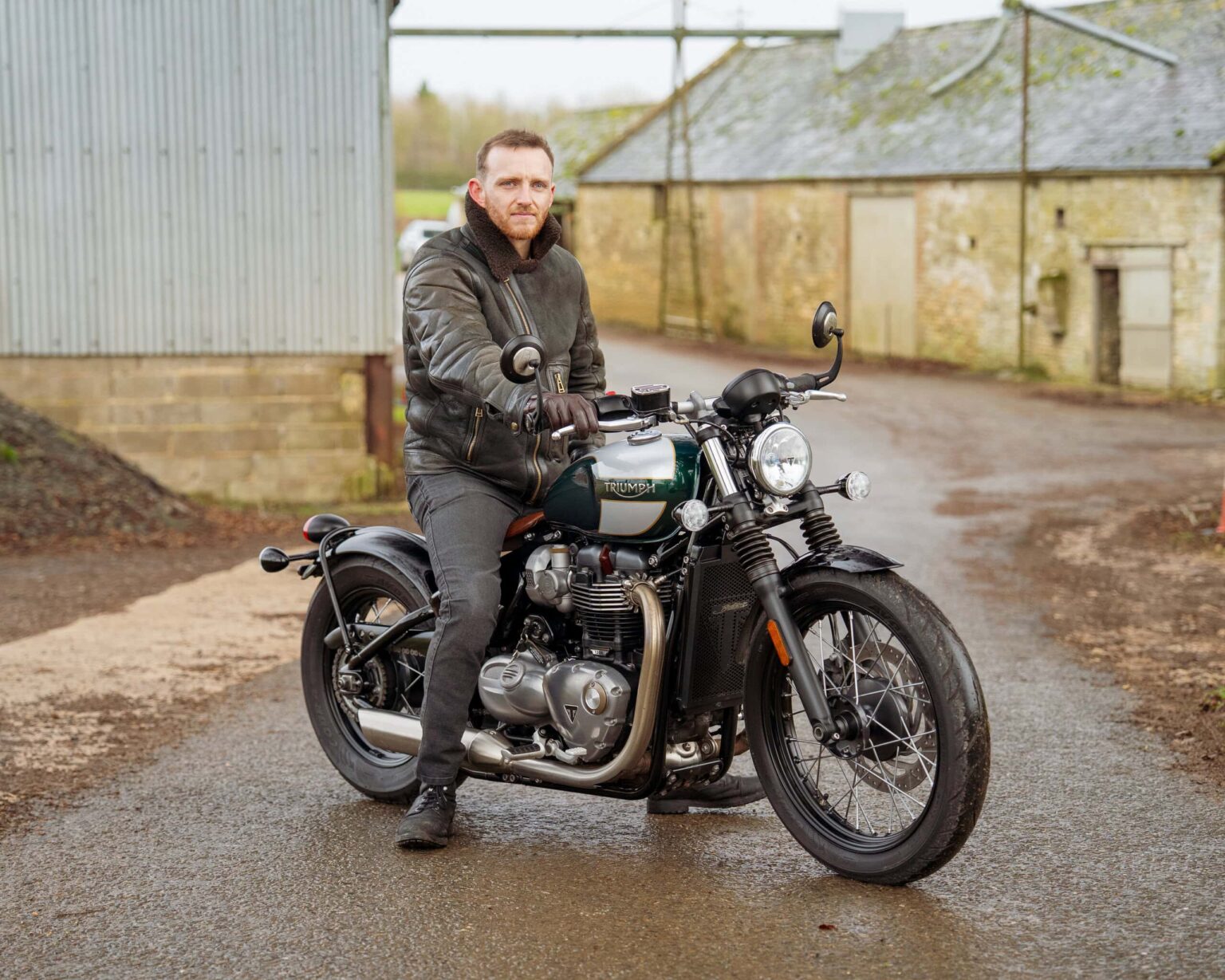 An image of a man sitting on a vintage-style motorcycle outside a rustic building, showcasing classi.