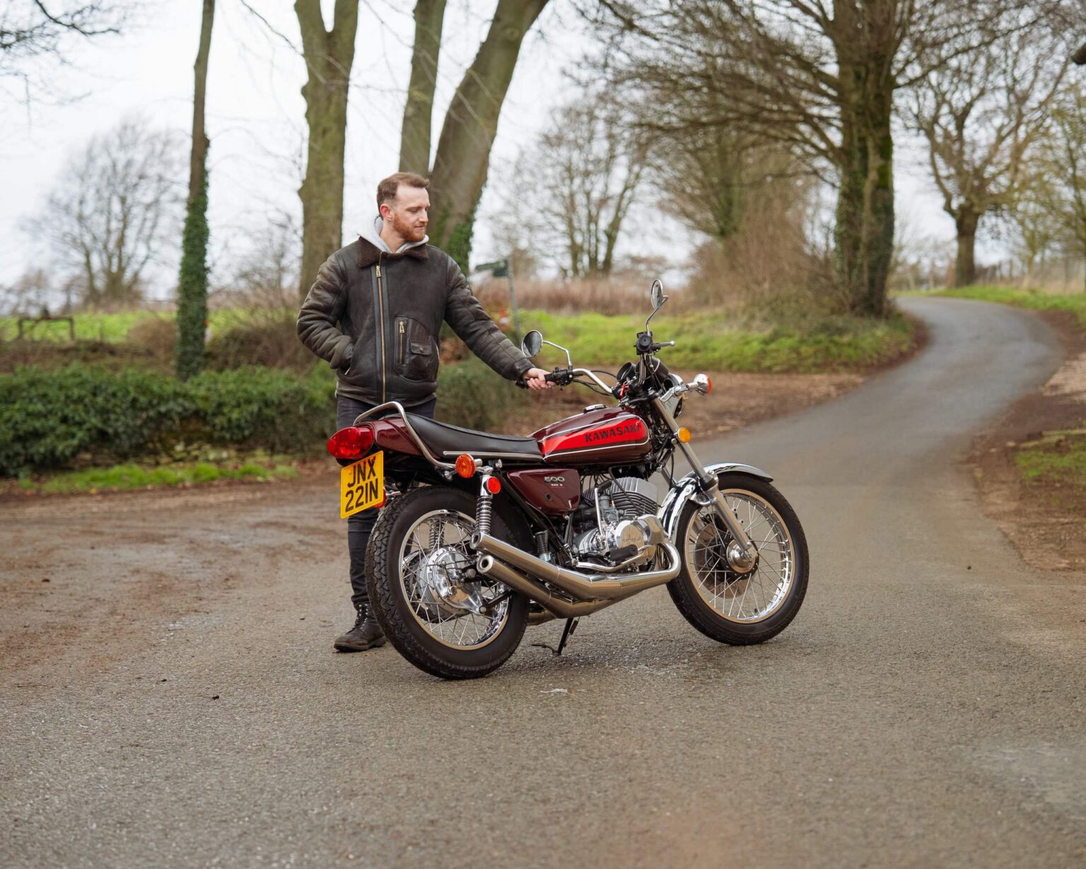 Motorcycle parked on a country road with a man standing beside it.