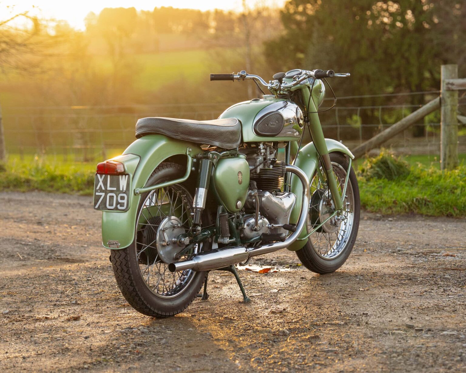 Vintage motorcycle with a green finish parked outdoors at sunset.