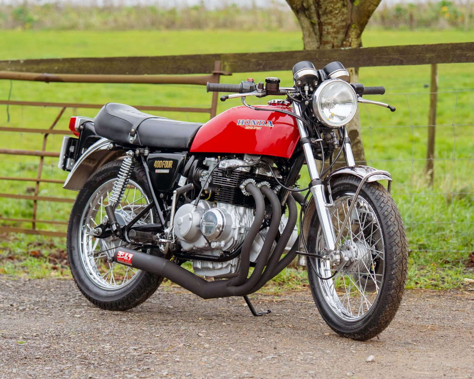 Motorcycle with red and black paint, vintage style, parked outdoors near a wooden fence.