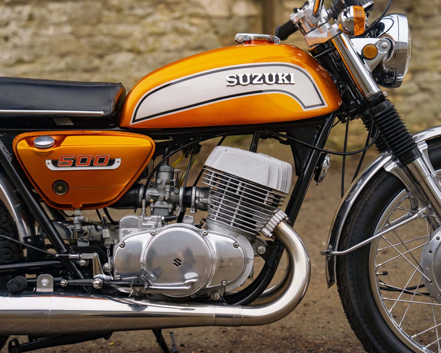 Vintage Suzuki 500 motorcycle with orange and white tank, detailed engine, and classic design.