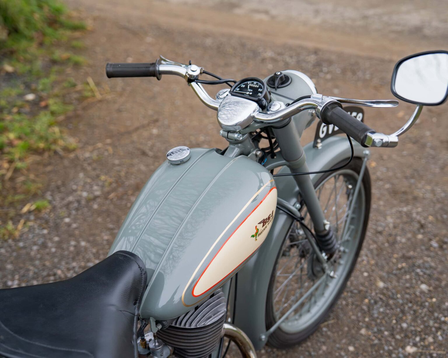 Vintage motorcycle with a grey fuel tank and chrome details, parked on a gravel path.