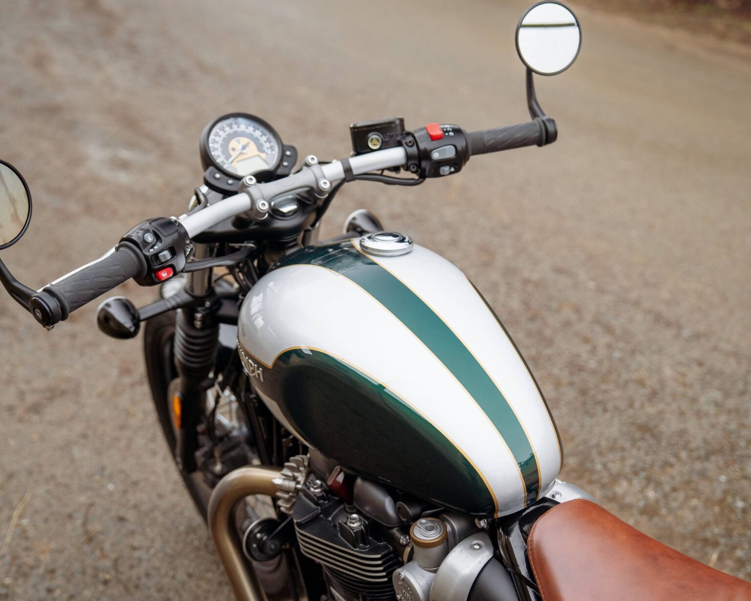 Motorcycle with vintage design and white-green fuel tank on a gravel road.