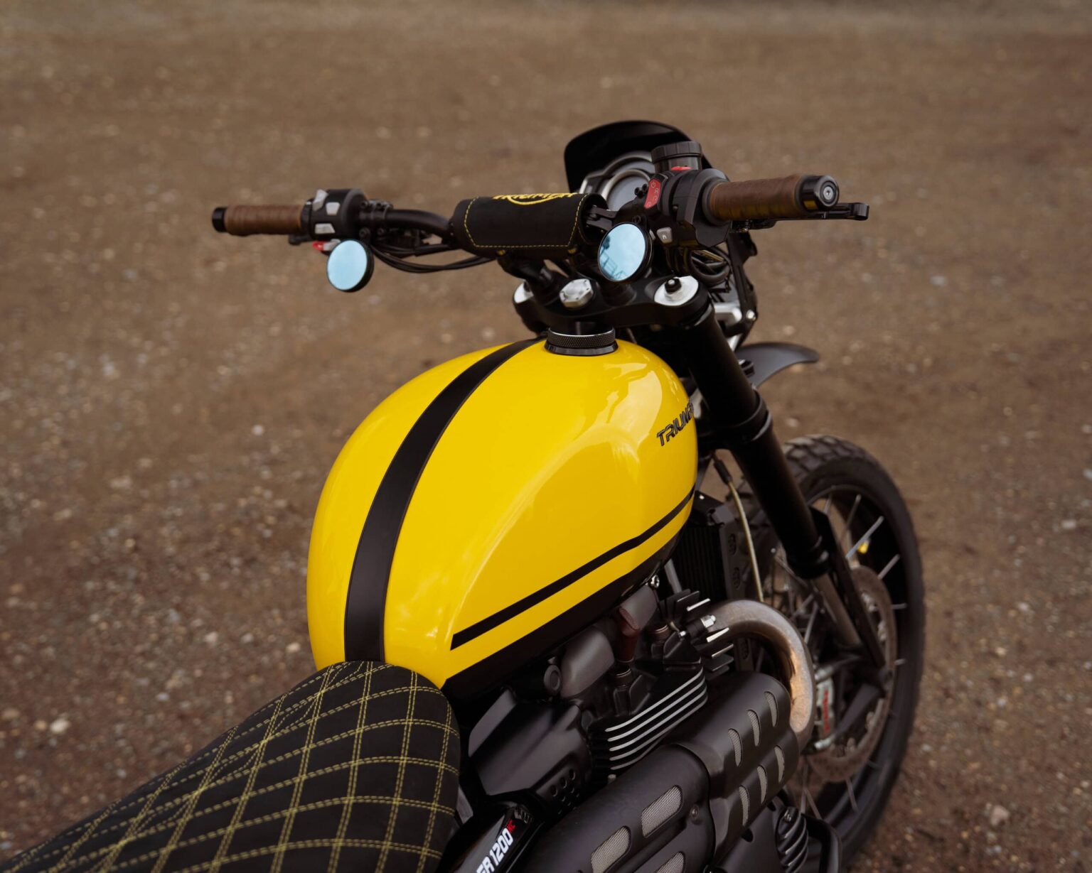 Motorcycle with yellow fuel tank and black racing stripes, parked on a gravel surface.