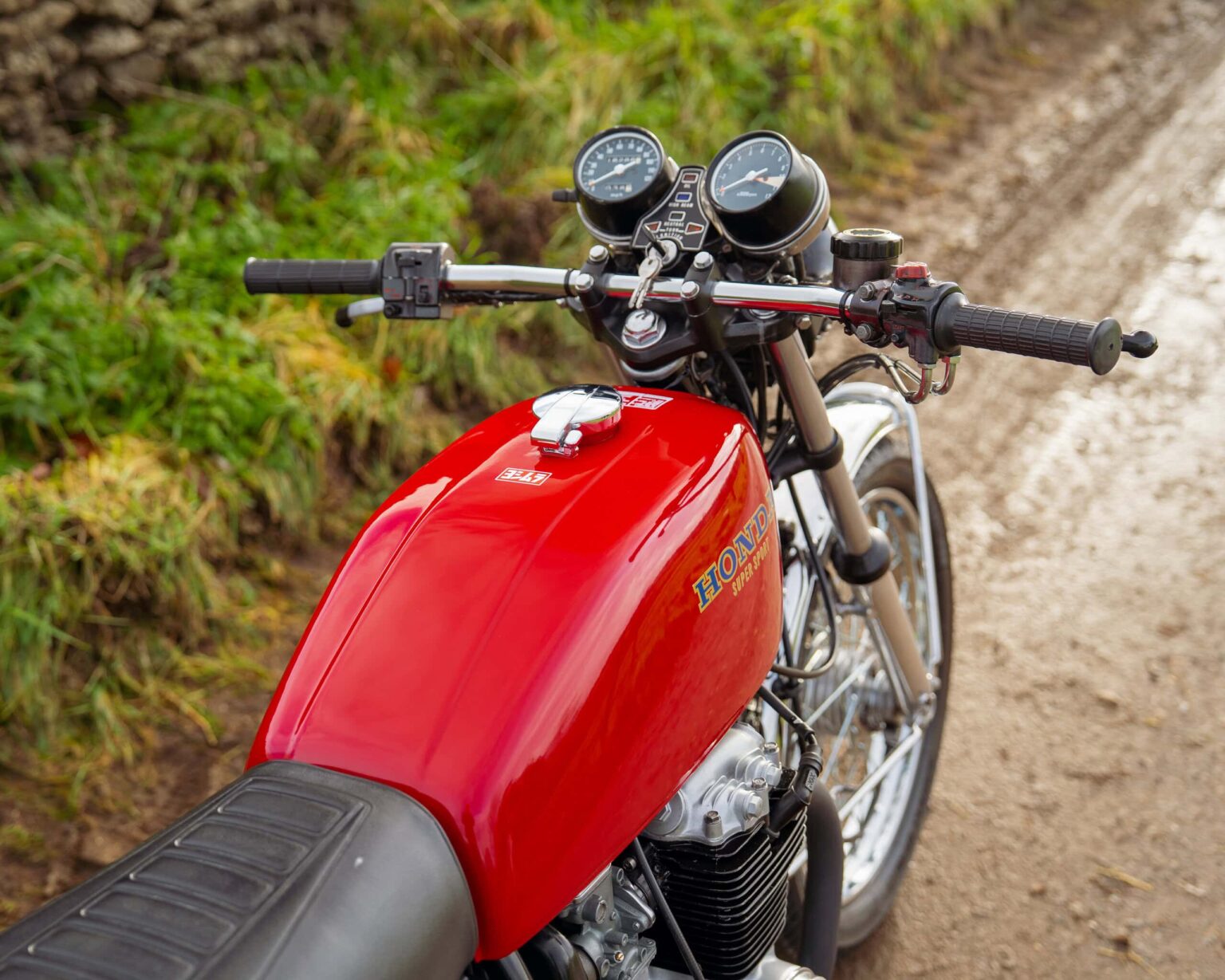 Red Honda motorcycle parked on a dirt track with greenery in the background.