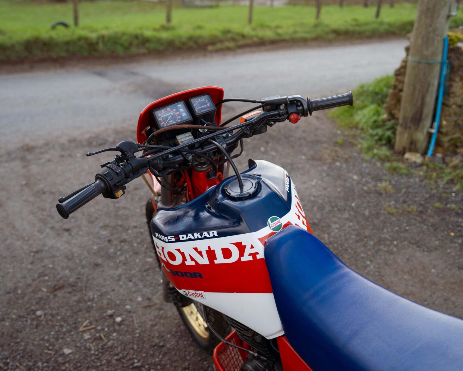 Honda Dakar motorcycle with a blue seat and dashboard, parked on a gravel path.