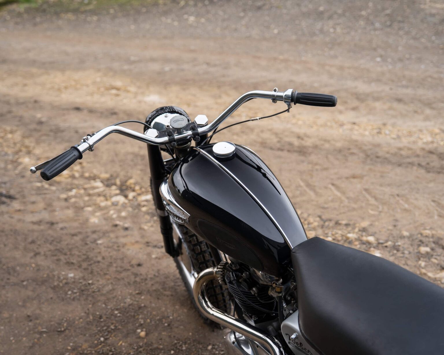 Motorcycle with black fuel tank and chrome handlebars on dirt terrain.