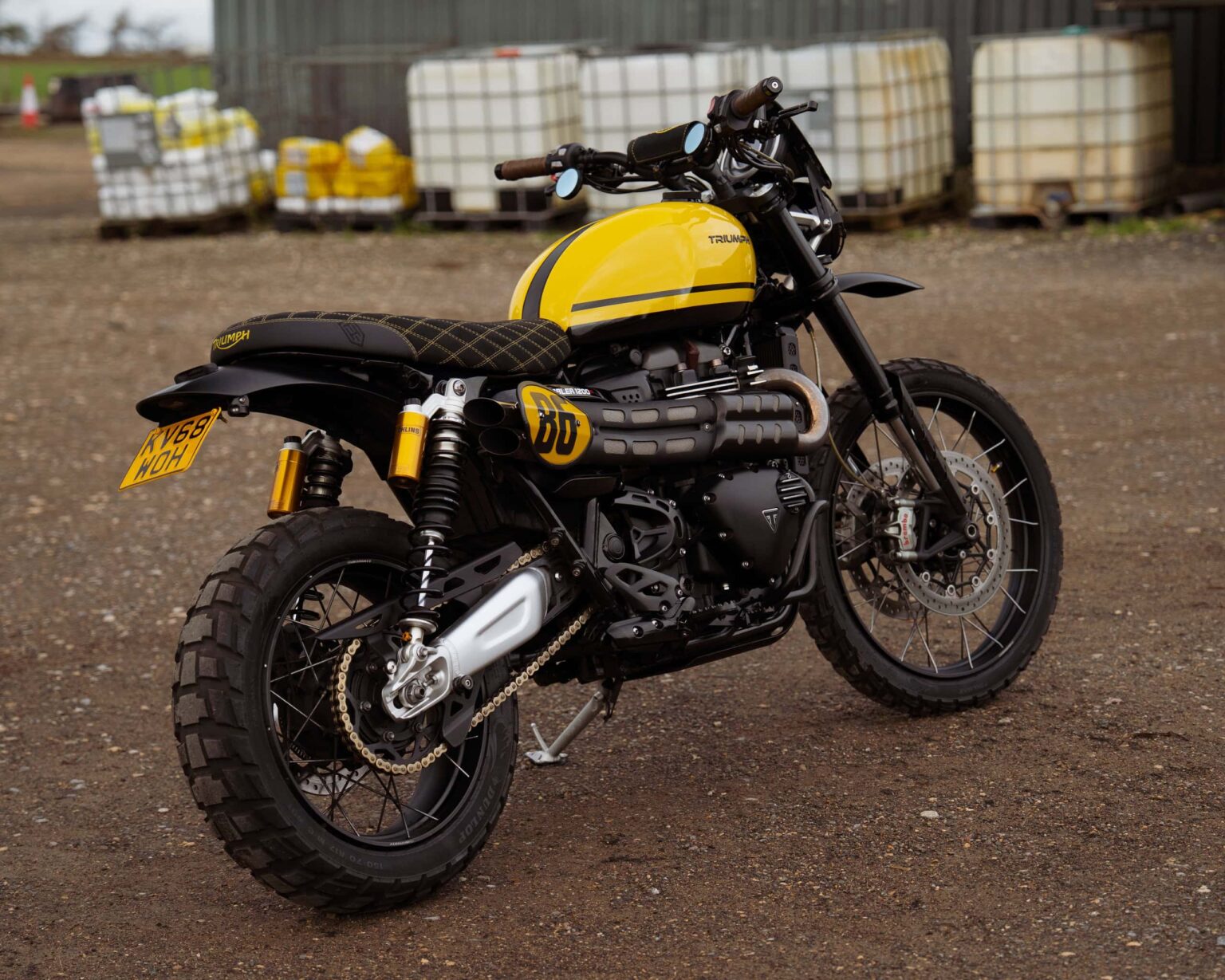 Motorcycle with yellow fuel tank and black frame, parked outdoors on dirt ground.