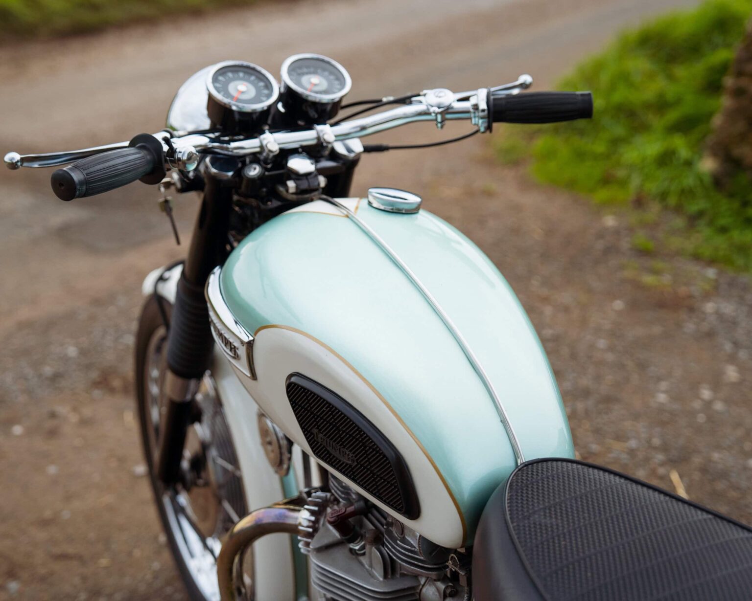 An elegant vintage motorcycle parked on a gravel path, showcasing its classic design and chrome deta.